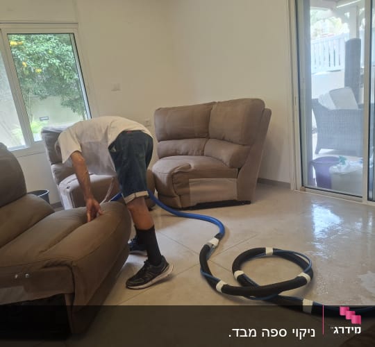 אדם מנקה ספה עם צינור מים בחדר מגורים
